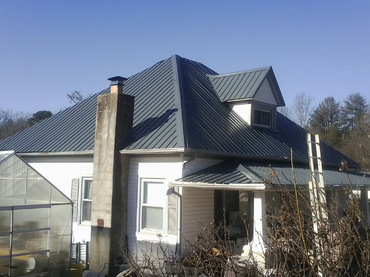 Dark blue standing seam metal roof on a white farmhouse with dormer — Slate & Tile Roof Repair by Roofing Brothers in Cresson