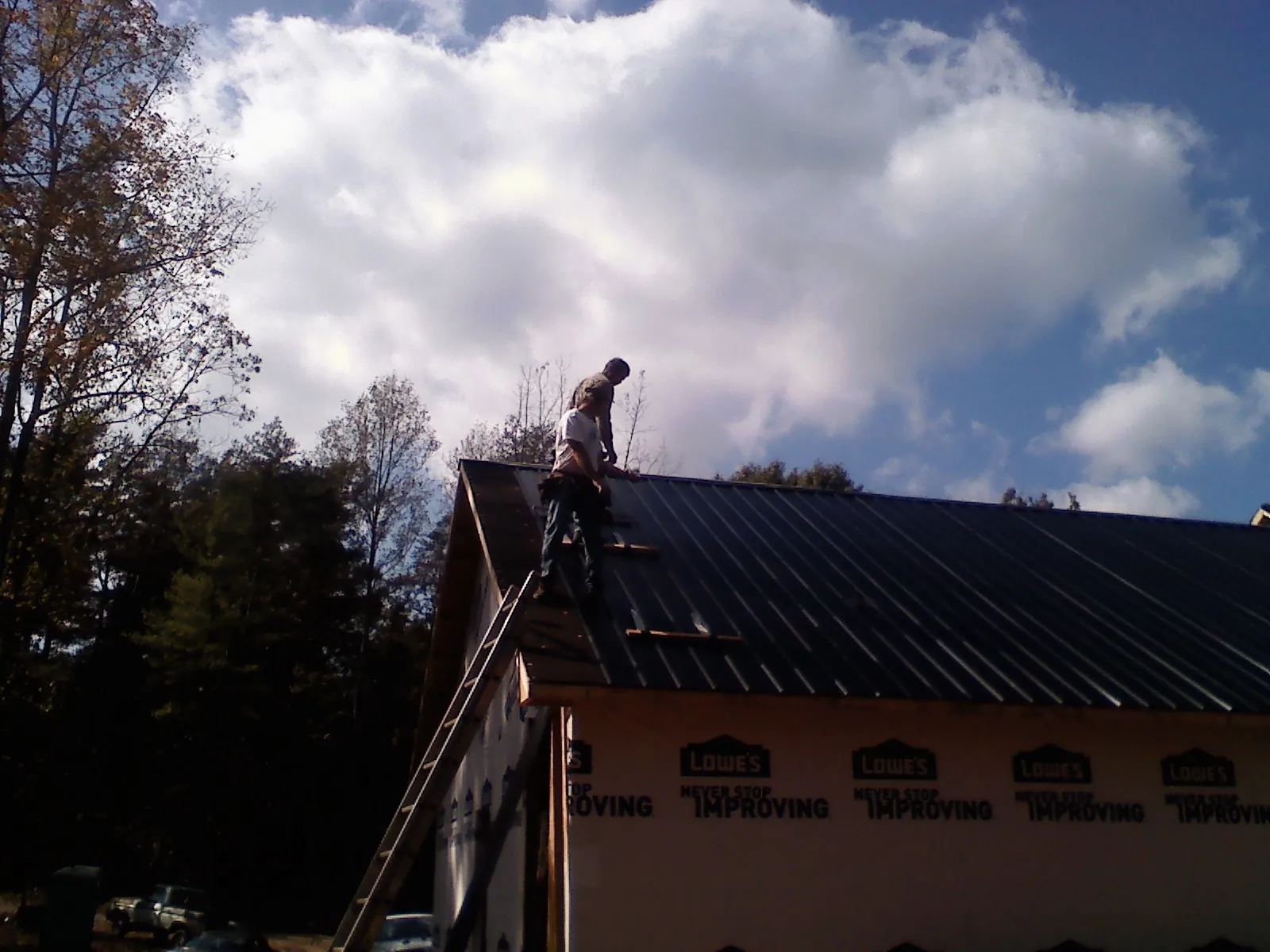 Roofer fastening dark metal panels high against a cloudy sky, from a Roof Inspection job in Cresson