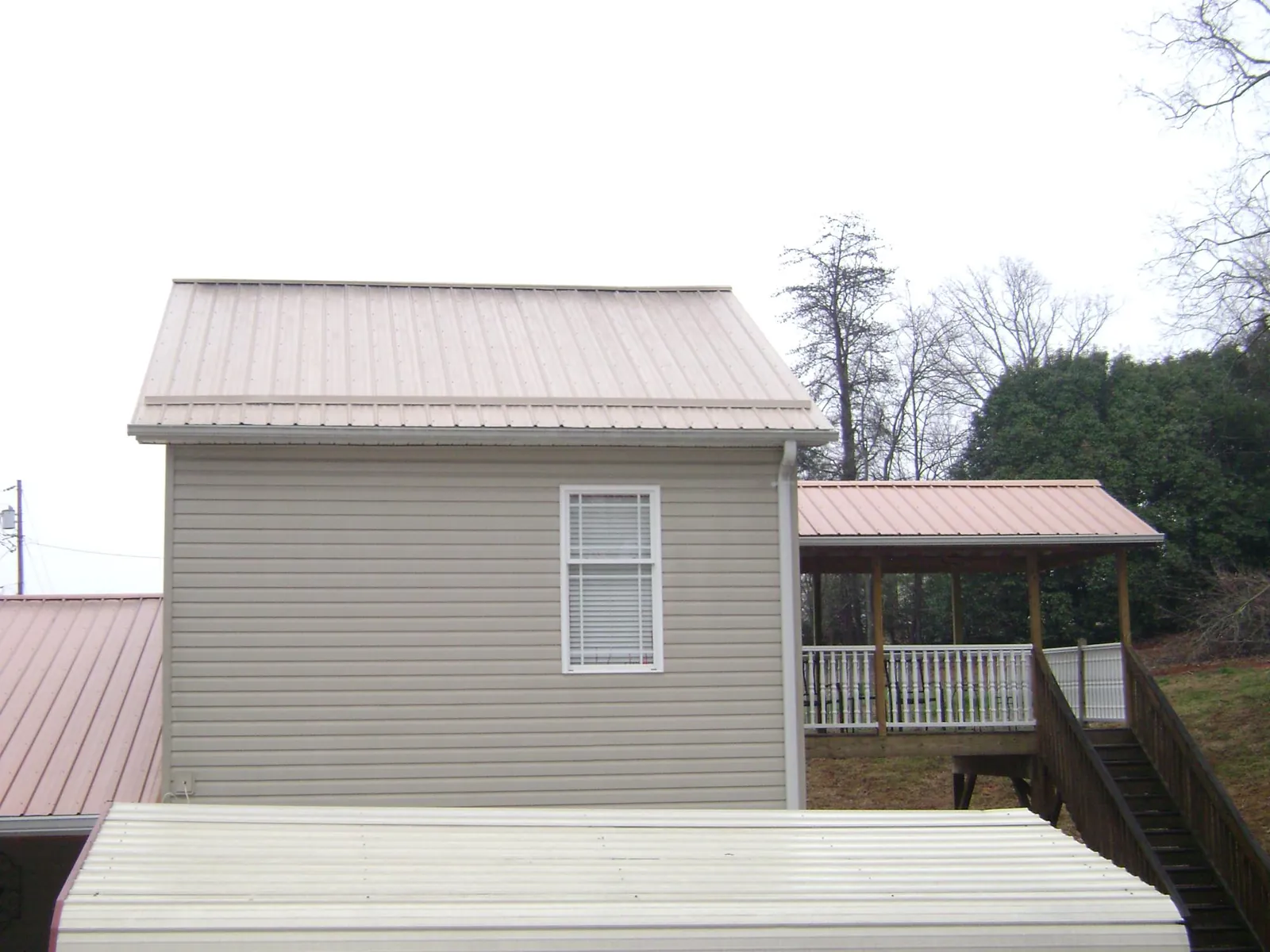 Tan metal roofs on a two story addition and attached porch, from a Roof Replacement job in Cresson